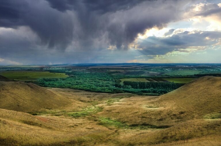 Scenic view of a valley with dramatic clouds over rolling hills, showcasing nature's beauty and tranquility.